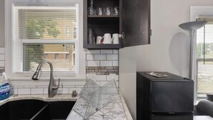 Une cuisine avec des meubles de couleur noire, un évier et une fenêtre avec des stores.