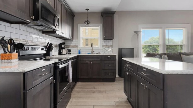 Une cuisine moderne avec des meubles de couleur sombre, une cuisinière en acier inoxydable et un grand îlot central.