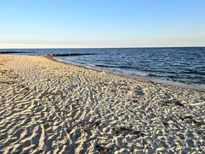 En sandstrand med milda vågor och klarblå himmel.