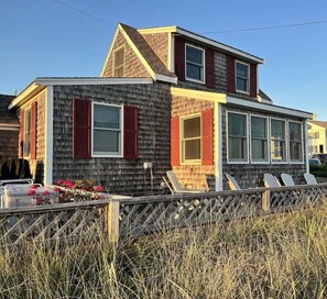 A two-story house with a sloped roof, red shutters, and a front porch with chairs.
