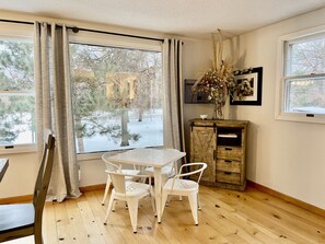 A room with a wooden floor, a white table with four chairs, a cabinet with a cross design, and a window with curtains. - Beautiful Farmhouse Style Country Home with Indoor Pool! (New Richmond)