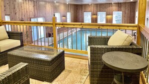 A wooden interior with a pool, wicker furniture, and a balcony with a railing. - Beautiful Farmhouse Style Country Home with Indoor Pool! (New Richmond)