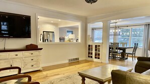 A spacious living room with a wooden coffee table, a television mounted on the wall, and a dining area with a table and chairs. - Beautiful Farmhouse Style Country Home with Indoor Pool! (New Richmond)