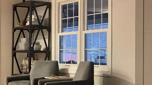 A room with two grey armchairs, a black shelving unit with dishes, and a window with a view of a snowy landscape. - Beautiful Farmhouse Style Country Home with Indoor Pool! (New Richmond)
