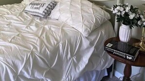Un dormitori amb llit, una taula de nit, una làmpada i un quadre floral a la paret.