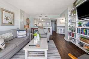 A living room with a sofa, coffee table, and bookshelf. - Luxury, condo w/oceanfront panoramic views, indoor pool, Jacuzzi, and private rooftop terrace (North Myrtle Beach)