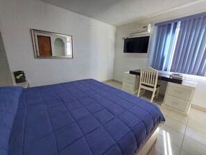 A bedroom with a bed, a desk, a chair, a television, and a window with blinds. - Hn Hotel (Durango)
