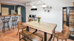 A dining area with a wooden table, four bar stools, a vase with flowers, a coffee machine, and a wine rack.