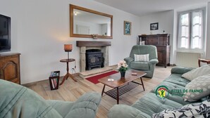 Una sala de estar con chimenea, sillones verdes, un sofá, una mesa de centro y un televisor.