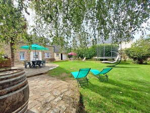 A backyard with a stone patio, a table with chairs, a trampoline, and a green lawn. - Au Vieux Cupidon - Josselin (JOSSELIN)