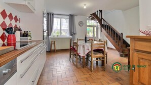 Una cocina con piso de parquete, un comedor con mesa y sillas de madera, y una escalera que sube a otro nivel.