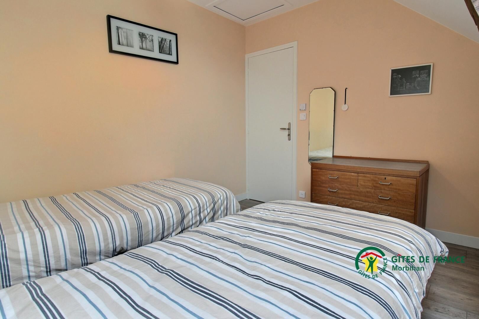 Une chambre à coucher avec un lit, une commode, une porte et un tableau encadré au mur.