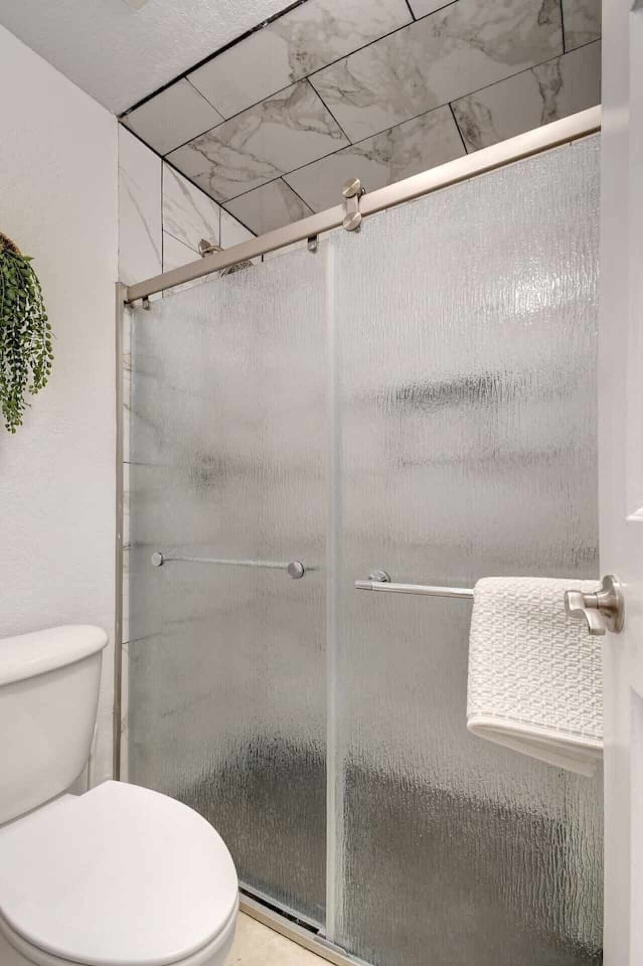 Un baño con inodoro blanco, cabina de ducha de vidrio y un perchero para toallas.