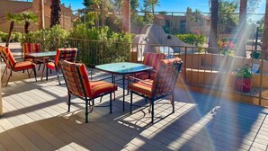 Une terrasse extérieure avec des tables et des chaises, entourée de palmiers et d’une clôture.