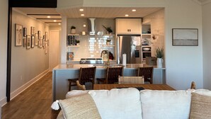 A modern living room with a light-colored sofa, wooden flooring, and a kitchen in the background. - Beachfront w/ Breathtaking Views! 1BR/2BA  Amenity Access included! (Seabrook Island)
