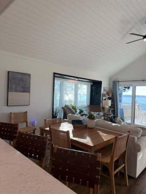 Uma sala de estar ampla com uma mesa de jantar, cadeiras, sofá e ventoinha no teto.