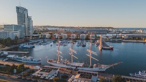 Ein Yachthafen mit zahlreichen Booten, darunter auch Segelschiffen, liegt neben einer modernen Skyline mit Wolkenkratzern.