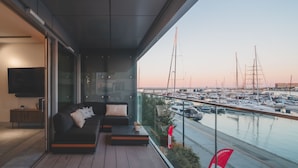 Ein modernes Wohnzimmer mit einer Couch und einem Couchtisch, einem an der Wand montierten Fernseher und Blick auf eine Marina mit Booten.