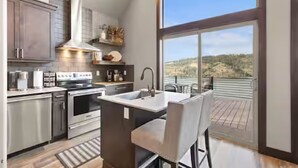 A modern kitchen with stainless steel appliances, a large island with a sink, and a view of a hilly landscape through a large window. - CDA Lakeview Escape (Harrison)