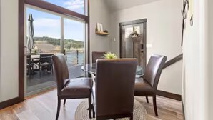 A dining area with a round table and four chairs, large windows with a view of the outdoors, and a door leading to another room. - CDA Lakeview Escape (Harrison)