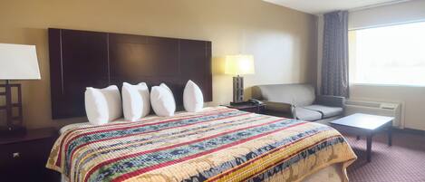 A hotel room with a large bed, a bedside table with a lamp, a chair, and a window with curtains.