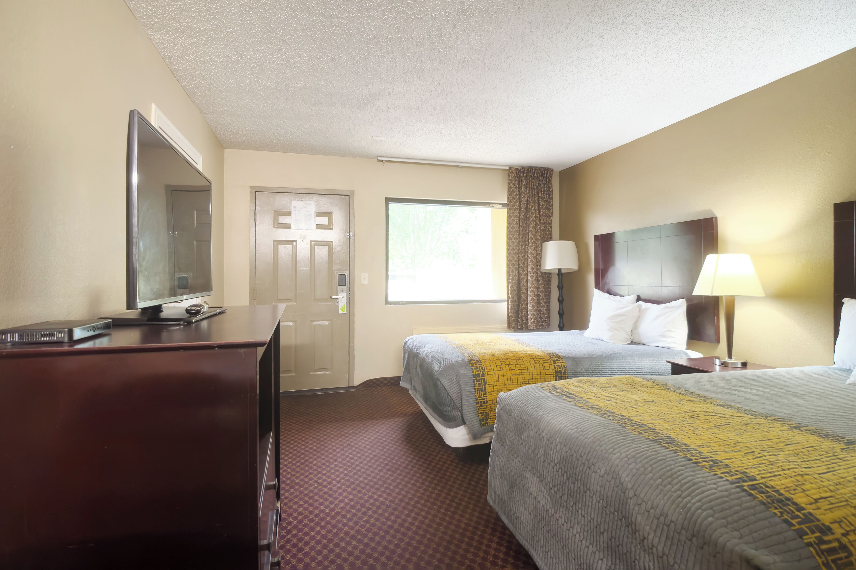 A hotel room with two beds, a desk with a computer, a mirror, a window with curtains, and a lamp.