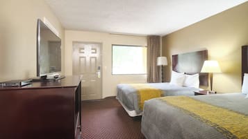 A hotel room with two beds, a desk with a computer, a mirror, a window with curtains, and a lamp.