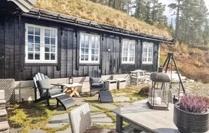 A wooden cabin with a thatched roof, outdoor seating area with chairs and tables, and a lantern. - 3 bedroom nice home in Eggedal (Eggedal)