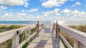Un paseo marítimo de madera que lleva a una playa con cielo despejado y nubes.