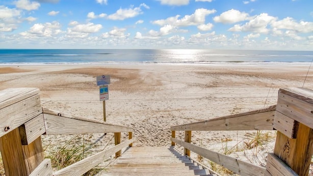 Una escalera de madera que conduce a una playa arenosa bajo un cielo despejado.