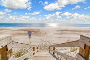 A wooden staircase leading to a sandy beach with a clear sky.