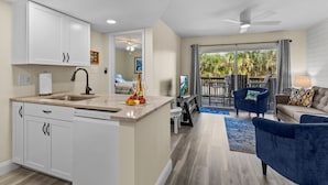 Una cocina moderna con armarios blancos, una isla central y un área de comedor con un sofá azul y un ventilador de techo.
