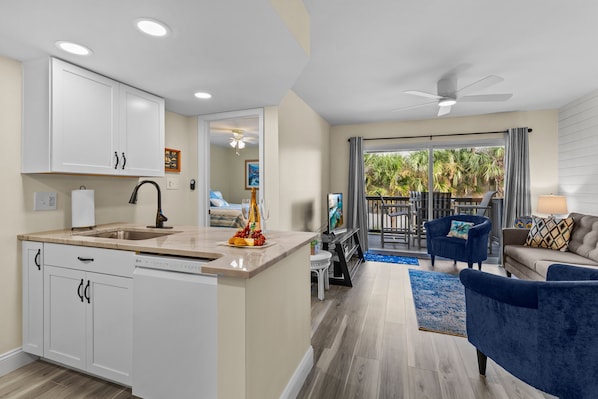 A modern kitchen with white cabinets, a central island, and a dining area with a blue sofa and a ceiling fan.