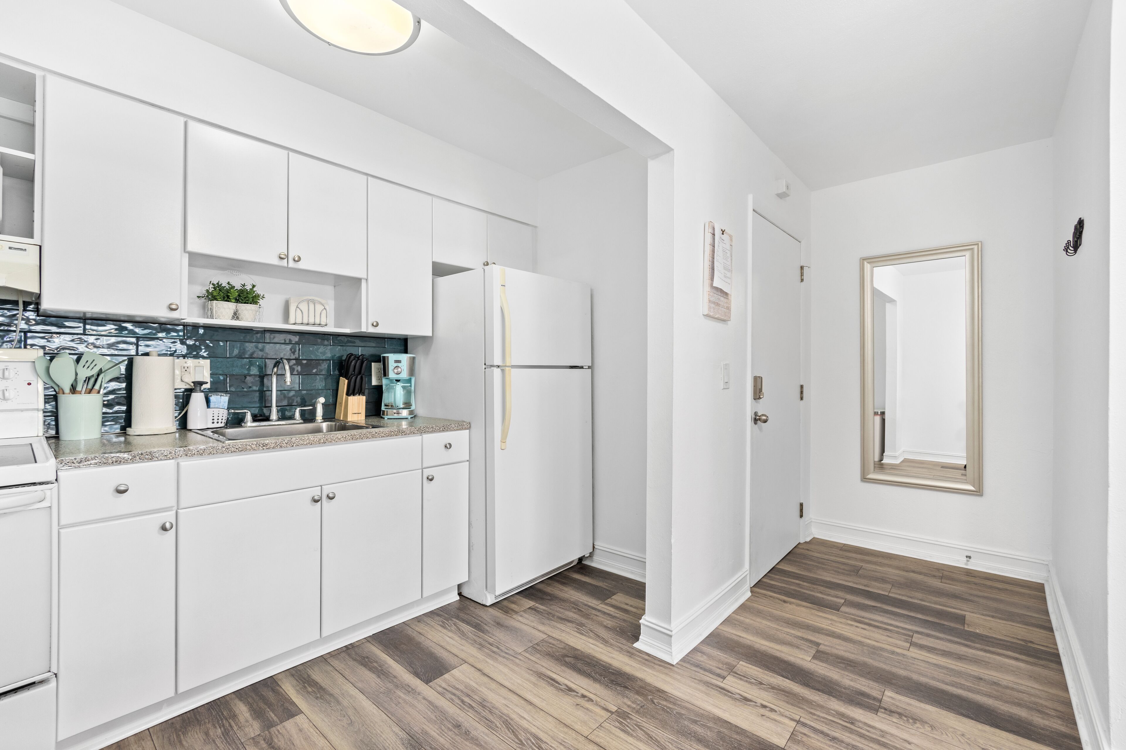 A modern kitchen with white cabinetry, a stainless steel refrigerator, and a wooden floor.