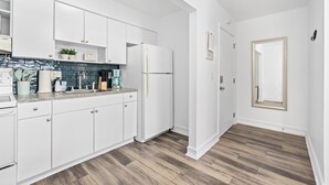 A modern kitchen with white cabinetry, a stainless steel refrigerator, and a wooden floor.