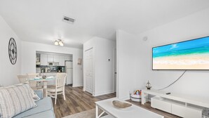 A modern living room with a TV, a sofa, a coffee table, and a kitchen in the background.