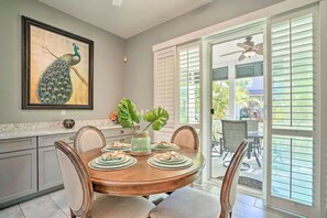A dining area with a round table set for four, a framed peacock painting on the wall, and a view of the outdoor patio through the sliding glass doors. - Coastal Ko' Olina Townhome - Walk to Beaches! (Kapolei)