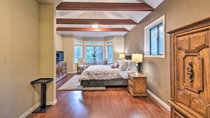 A bedroom with a large bed, a wooden cabinet, and a desk with a chair. There are windows and a ceiling fan. - Deck + Grill: Mtn Haven in Stanislaus Nat'l Forest (Arnold)