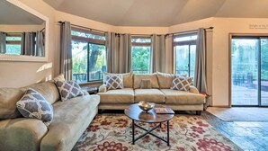 A cozy living room with a beige sofa, a coffee table, and a large window with curtains. - Deck + Grill: Mtn Haven in Stanislaus Nat'l Forest (Arnold)