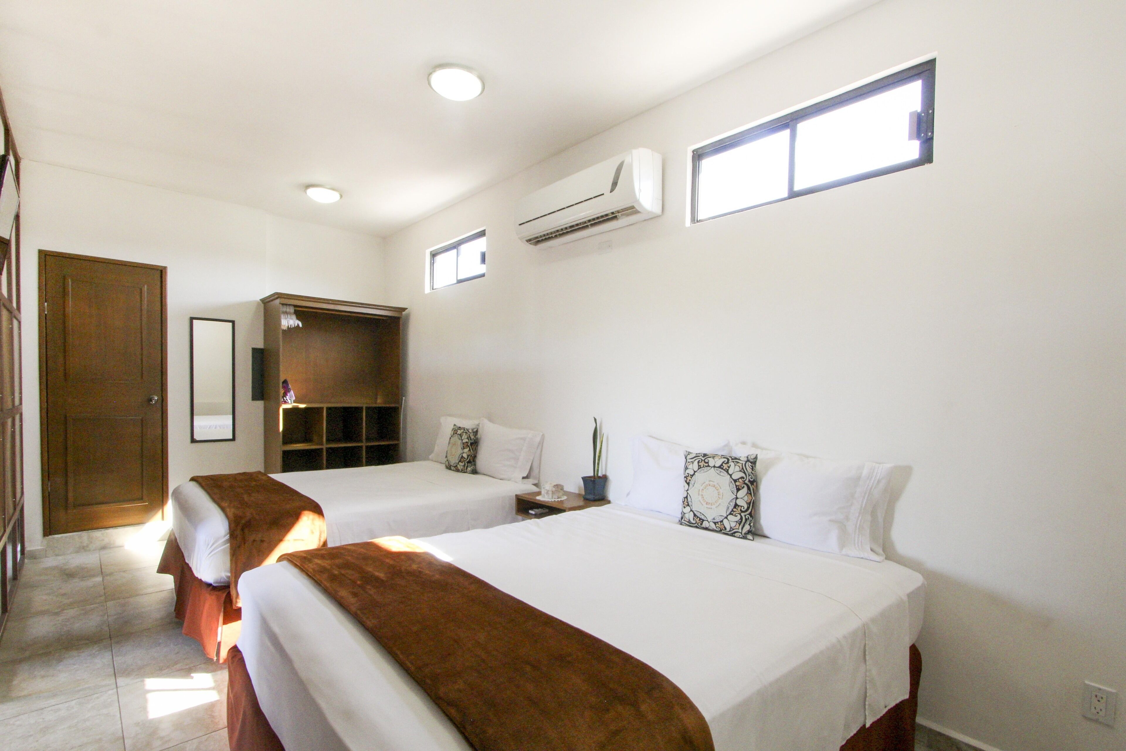 Une chambre d’hôtel avec deux lits, une armoire, un miroir et un appareil de climatisation.