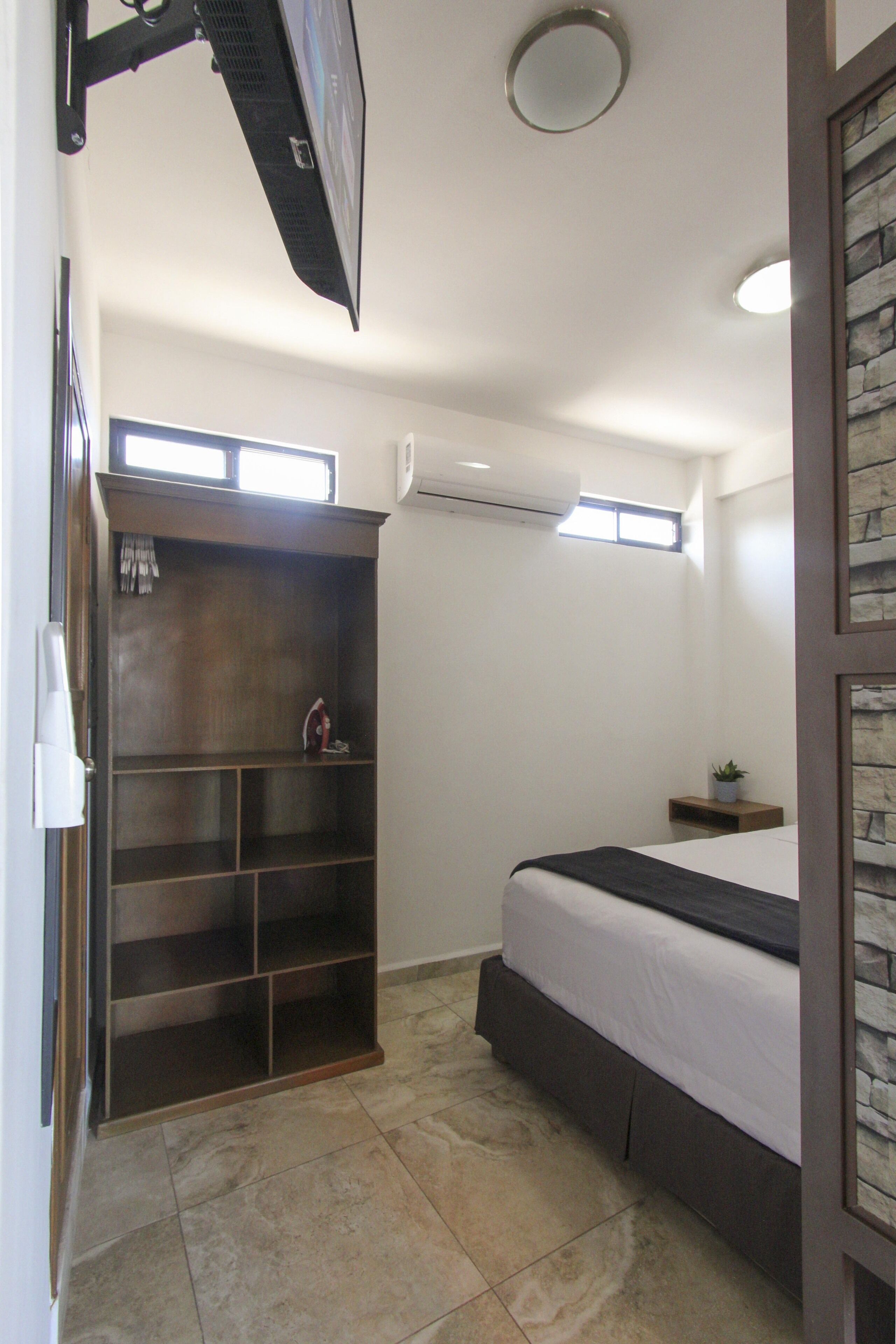 Quarto com cama, armário embutido, mesa de cabeceira pequena e uma janela.