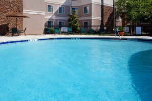 Relax by the pool, surrounded by lounge chairs and an umbrella, with a clear view of the adjacent building.