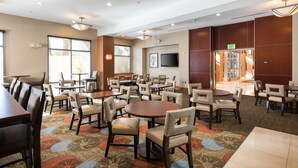 A hotel dining area with multiple tables and chairs, a flat-screen TV mounted on the wall, and an exit sign. - 1 Bedroom | FREE Breakfast + Pool Access & Hot Tub (Las Vegas)