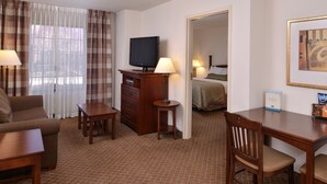 A hotel room with a sofa, a desk, a television, a dresser, and a bed. - Equipped Suite Near the Airport! Fitness Center + Free Breakfast (Plainfield)