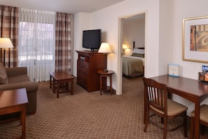 Ein Hotelzimmer mit Sofa, Schreibtisch, Fernseher, Kommode und Bett.