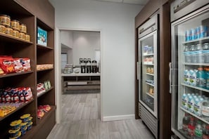 Un garde-manger avec des étagères remplies de collations et de boissons, un réfrigérateur et une machine à café.