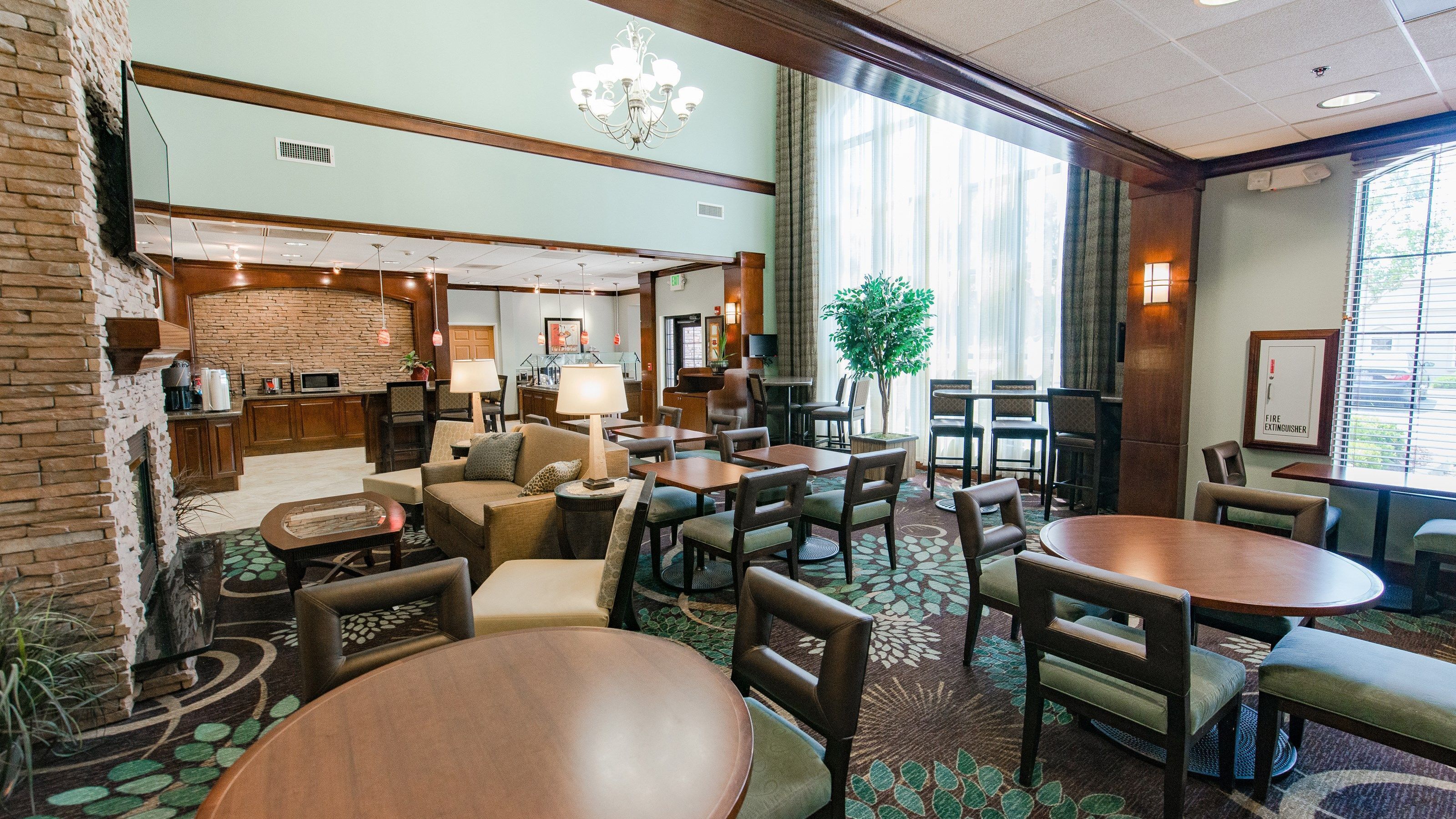 A hotel lobby with a fireplace, seating area, and a large window with blinds.