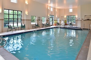 Ein Hallenbad mit klarem Wasser, umgeben von Fenstern und Liegestühlen.
