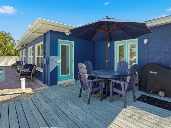 A deck with a table and chairs, a grill, and a pool.