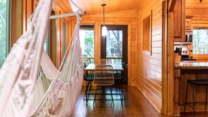 Ein Holzblockhaus-Interieur mit Hängematte, Esstisch, Stühlen und einer Küchenzeile.